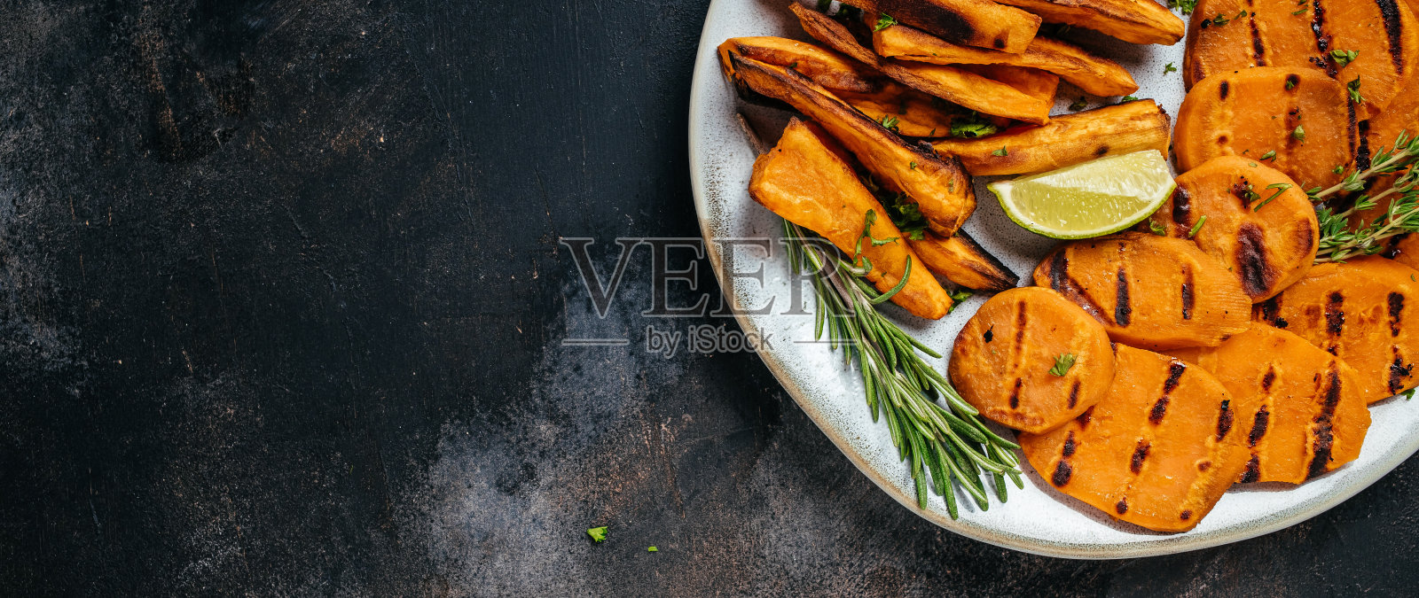 自制的烤橙色甘薯,配上酸橙和香草,放在深色背景的盘子里。长标题格式。俯视图照片摄影图片