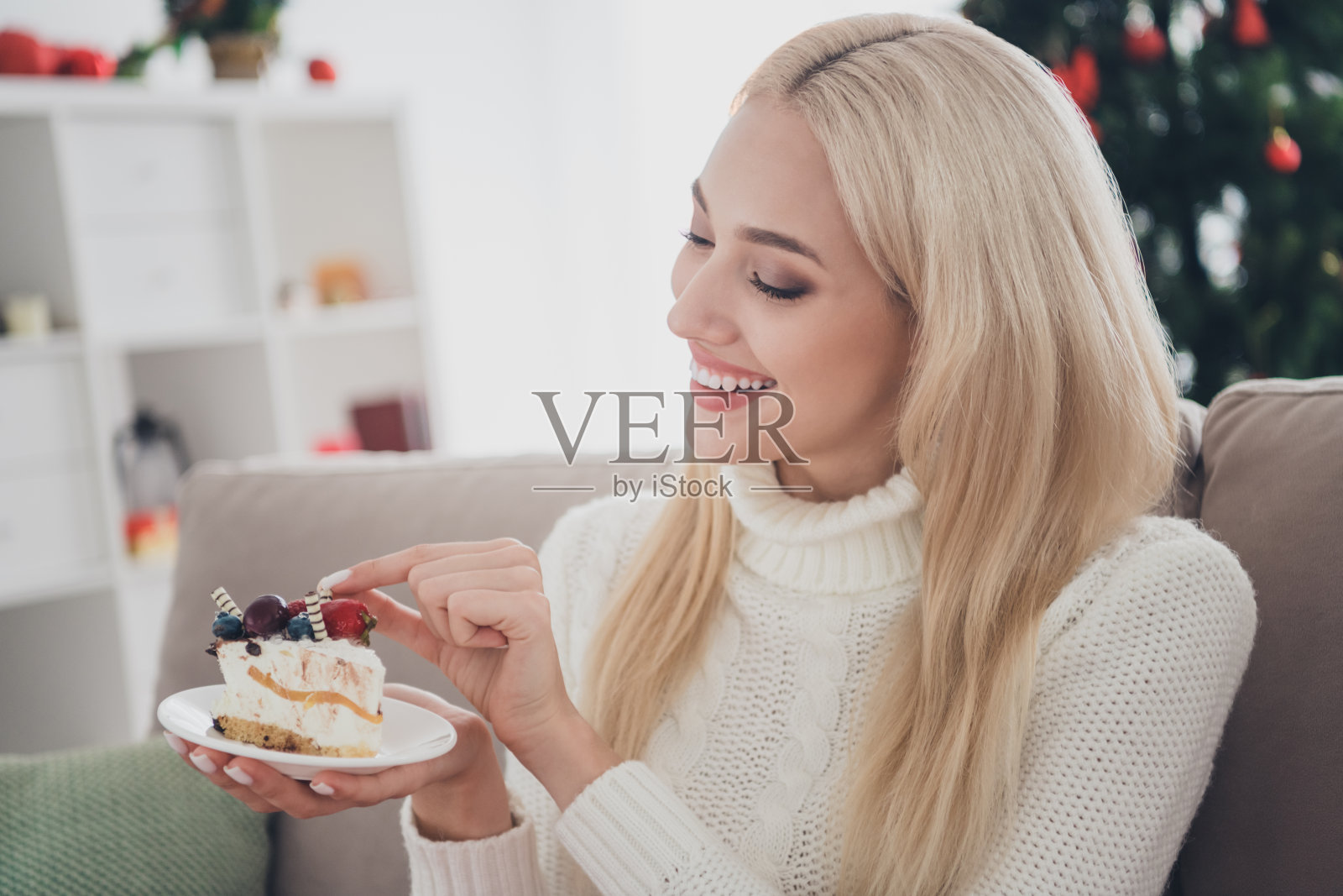 可爱迷人的年轻女士穿着针织套头衫,微笑着吃美味的甜点,室内,室内房间照片摄影图片