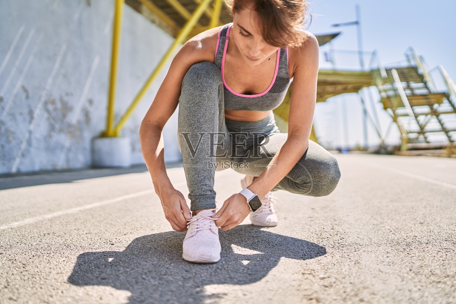 年轻的白人女子穿着运动服在街上系鞋照片摄影图片