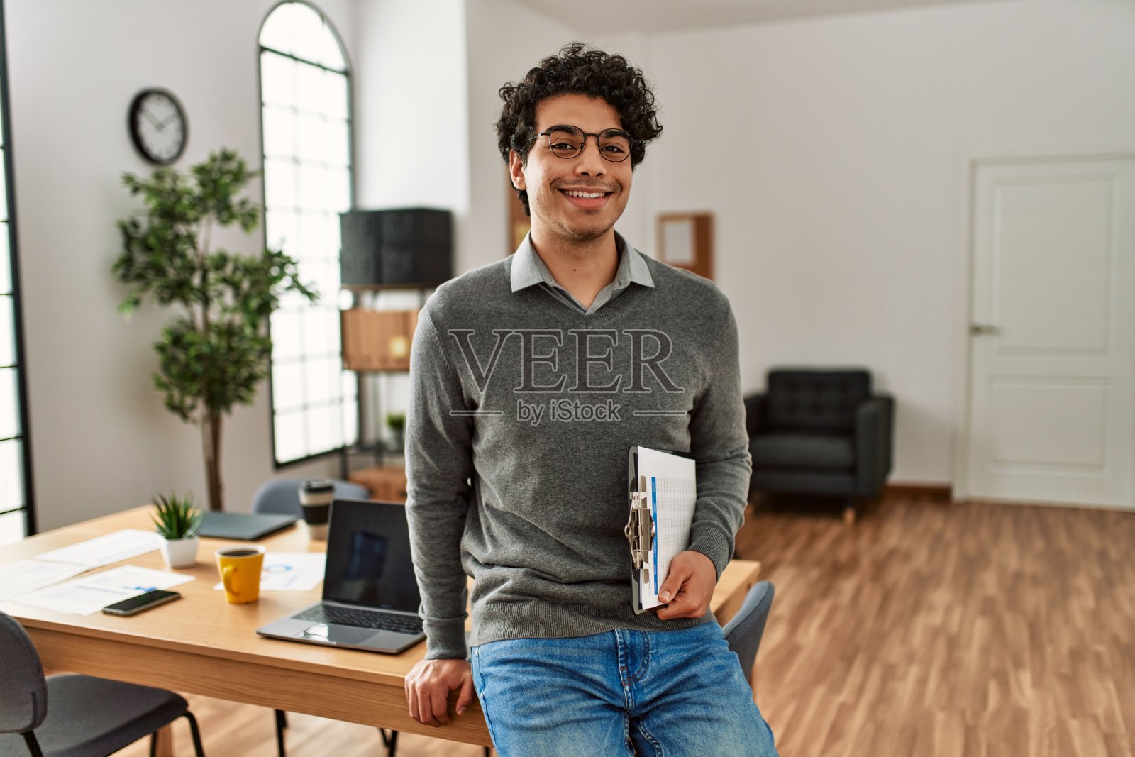 年轻的西班牙商人微笑着在办公室拿着写字板。照片摄影图片