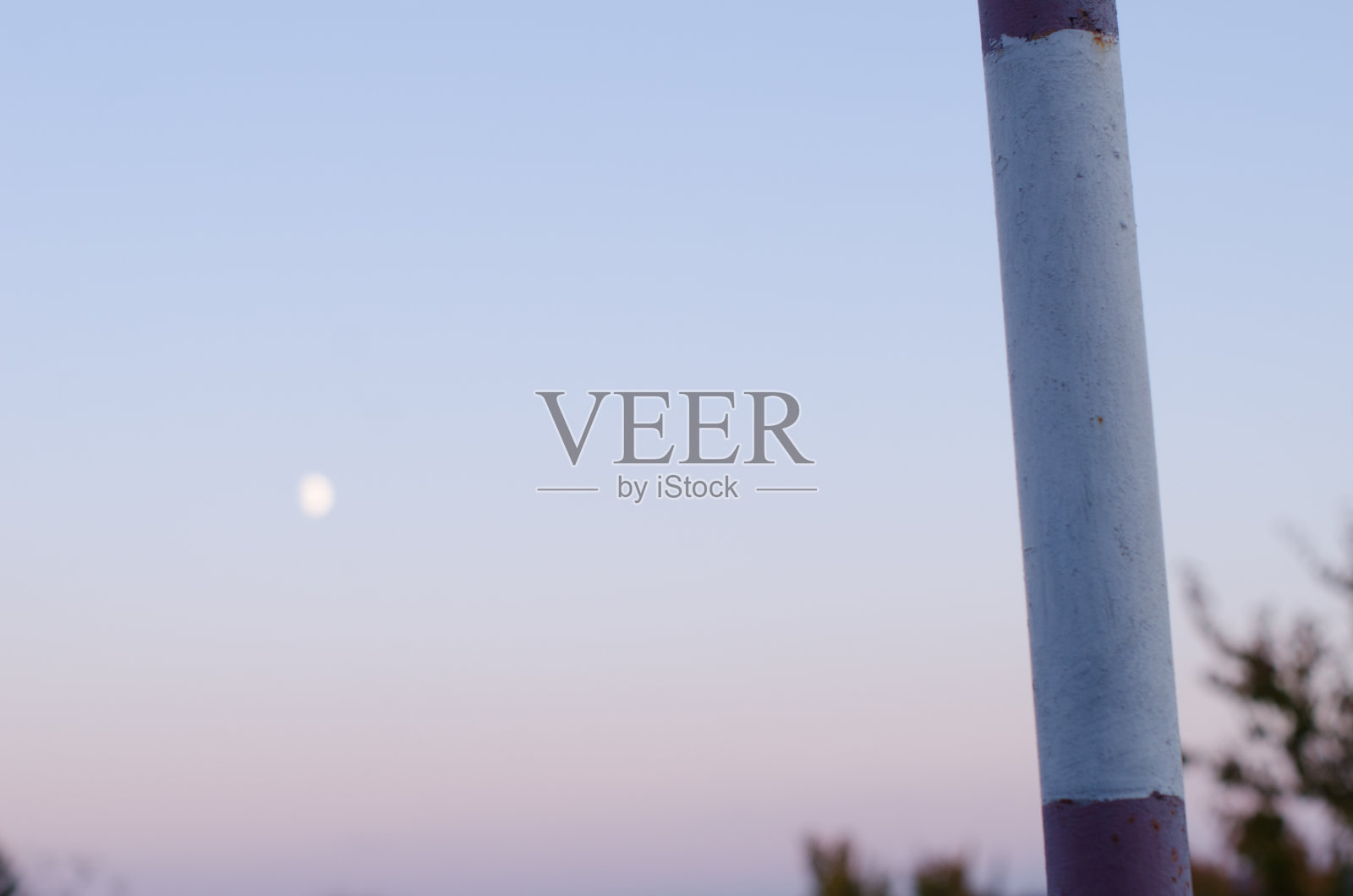 傍晚的背景是一个旧足球球门的金属管,漆成红白两色,美丽的天空和模糊的月亮。本空间照片摄影图片