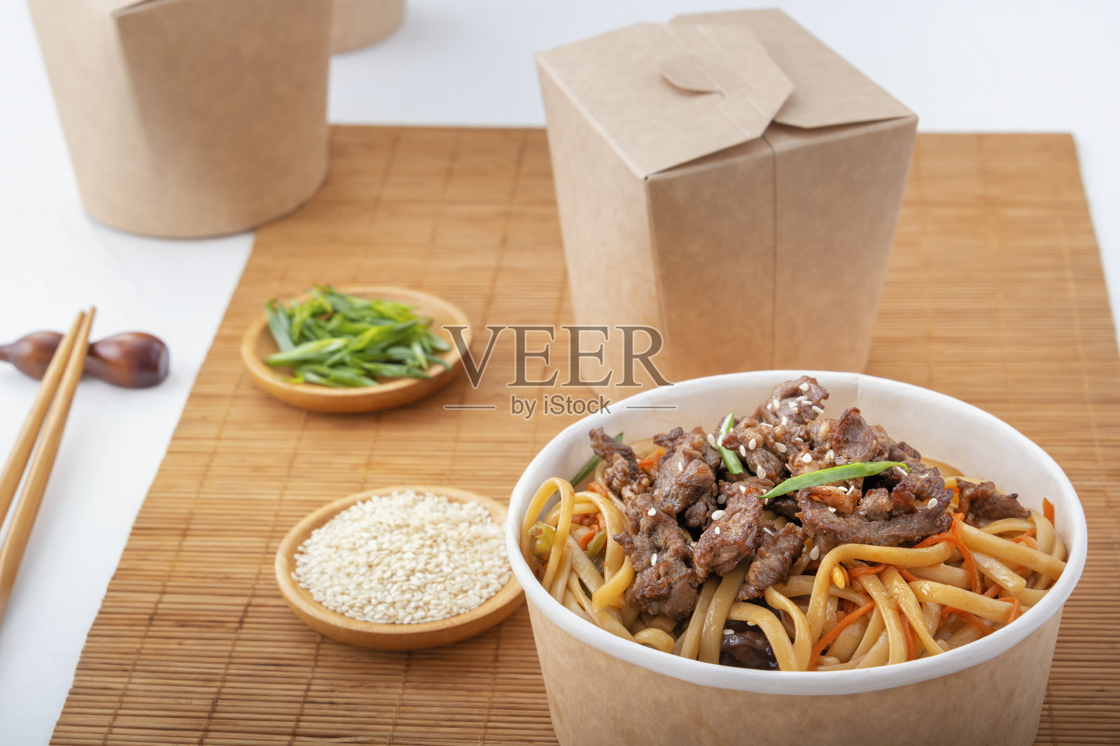 面条、肉、辣椒、香草和芝麻装在一次性纸盘里,背景是用筷子和纸盒送食物的垫子。照片摄影图片
