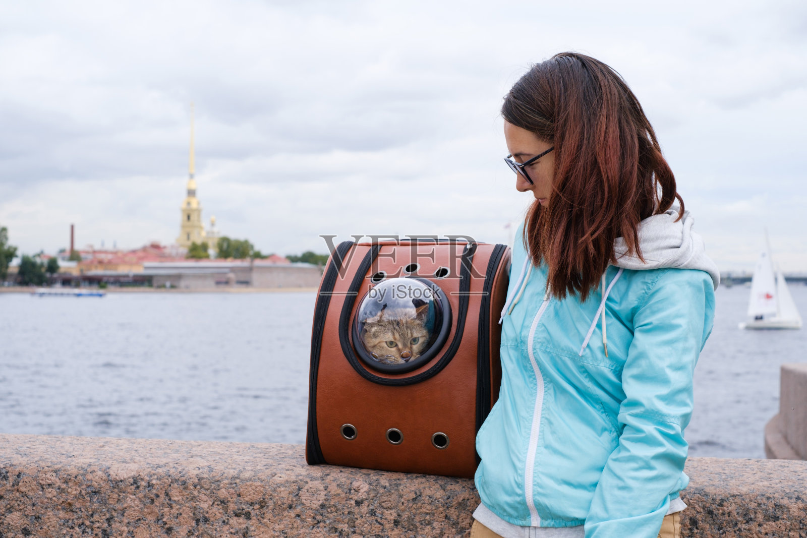 背包里的流浪猫和它的主人一起走在圣彼得堡的堤岸上。照片摄影图片