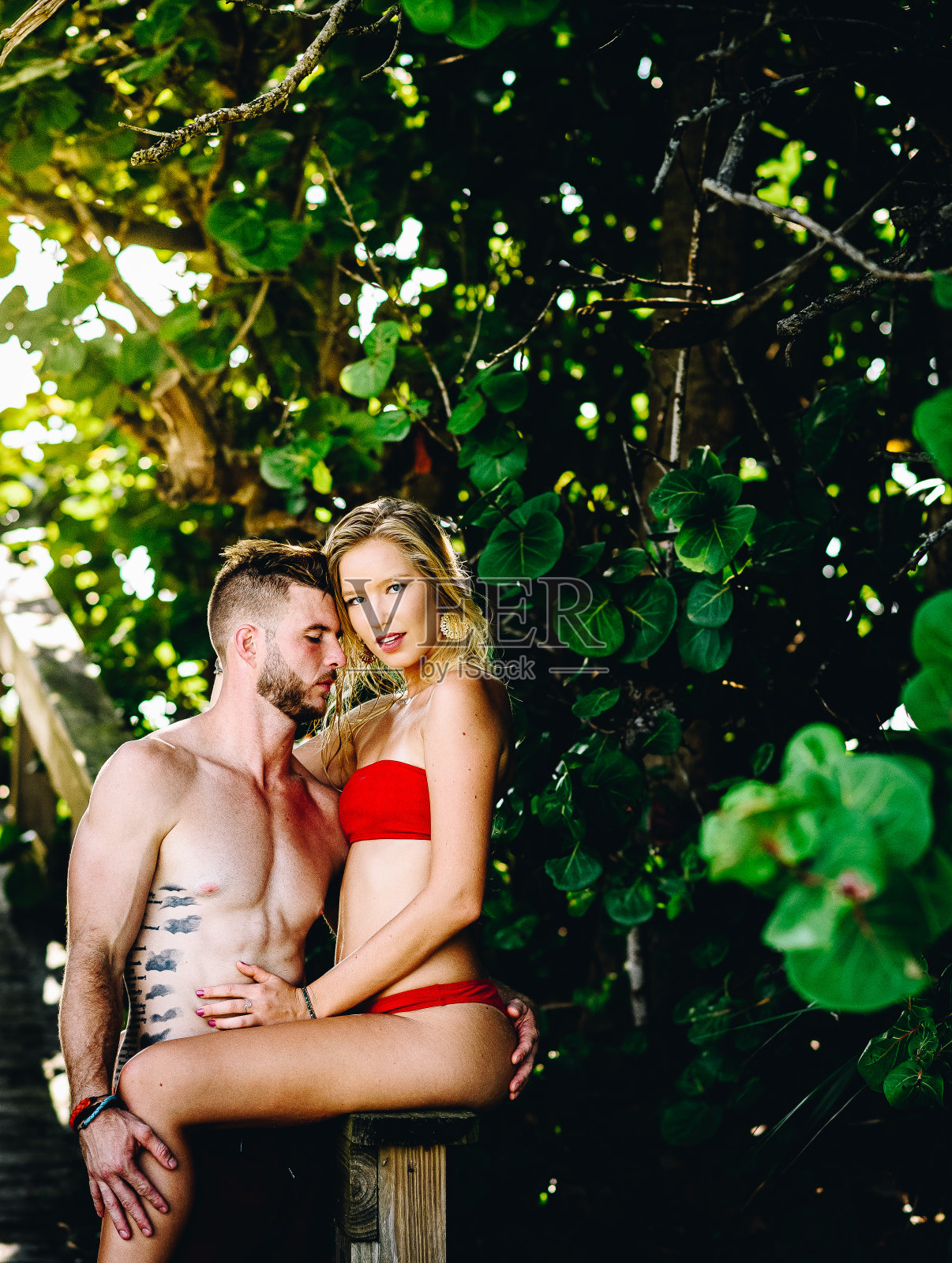 性感年轻的夏天情侣在热带田园诗般的海滩走道上,穿着红色泳装,手挽着手照片摄影图片