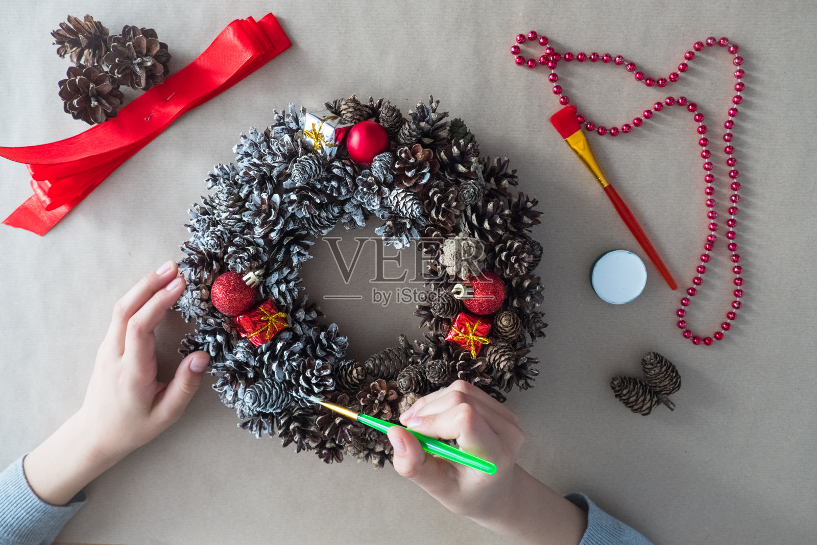 DIY。第3步俯视图花匠的手与刷子,圣诞花环杉木锥,装饰玩具照片摄影图片