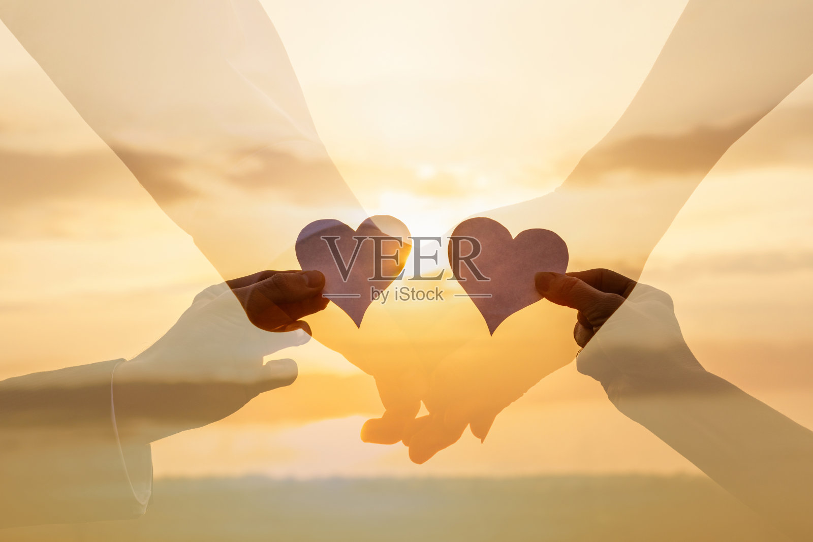 在阳光明媚的夕阳下,情侣们伸出纸上的心。照片摄影图片