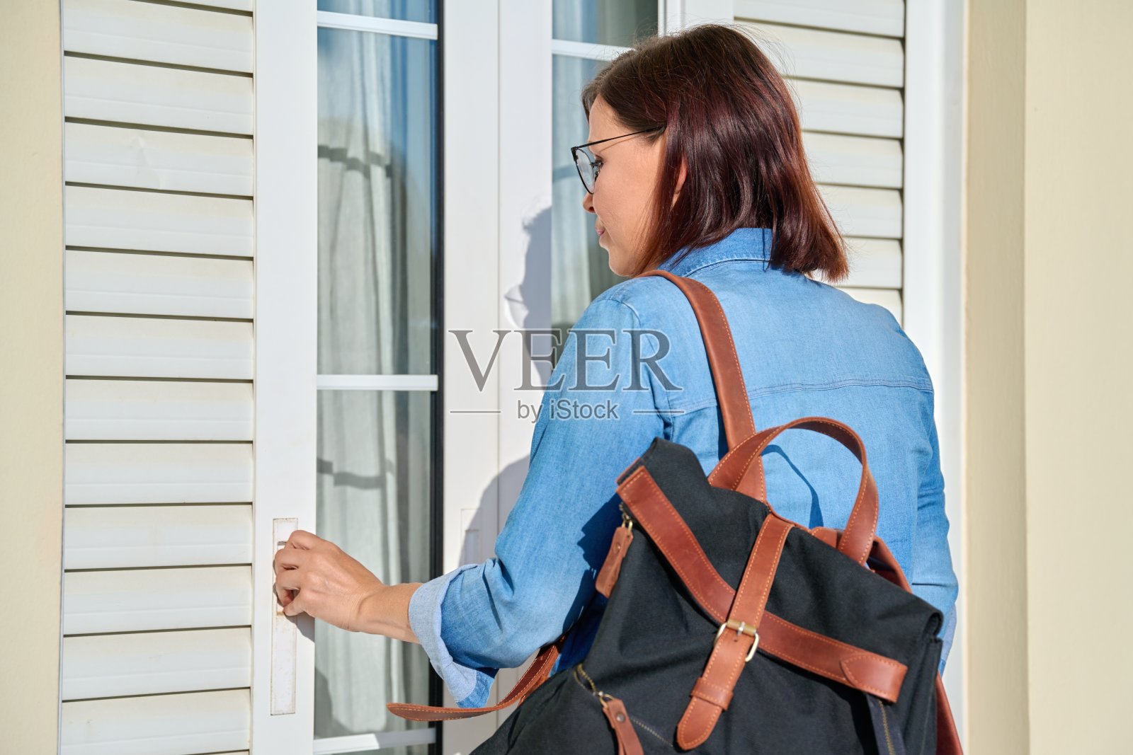 背着背包的女人打开窗户外的百叶窗照片摄影图片