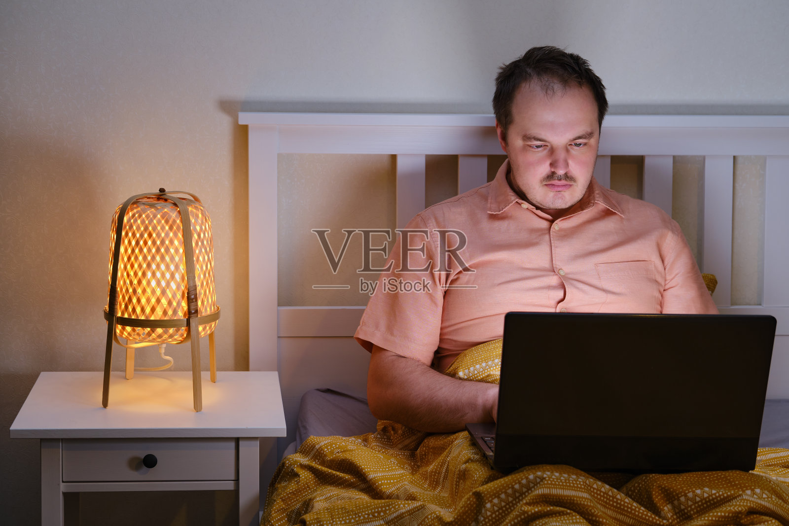 一个成年人坐在床上,在夜灯的灯光下,对着电脑工作照片摄影图片