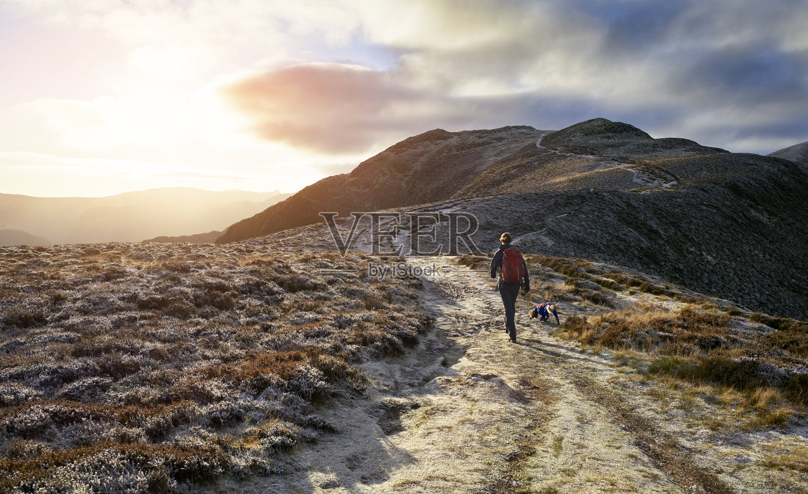 日出时分,一个徒步旅行者和他们的狗正从梅登荒原走向High Spy的山顶照片摄影图片