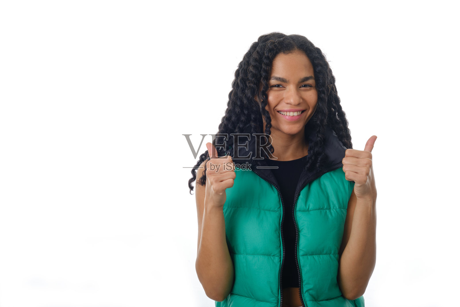 女人站在一个孤立的背景上,看着相机,竖起大拇指。照片摄影图片