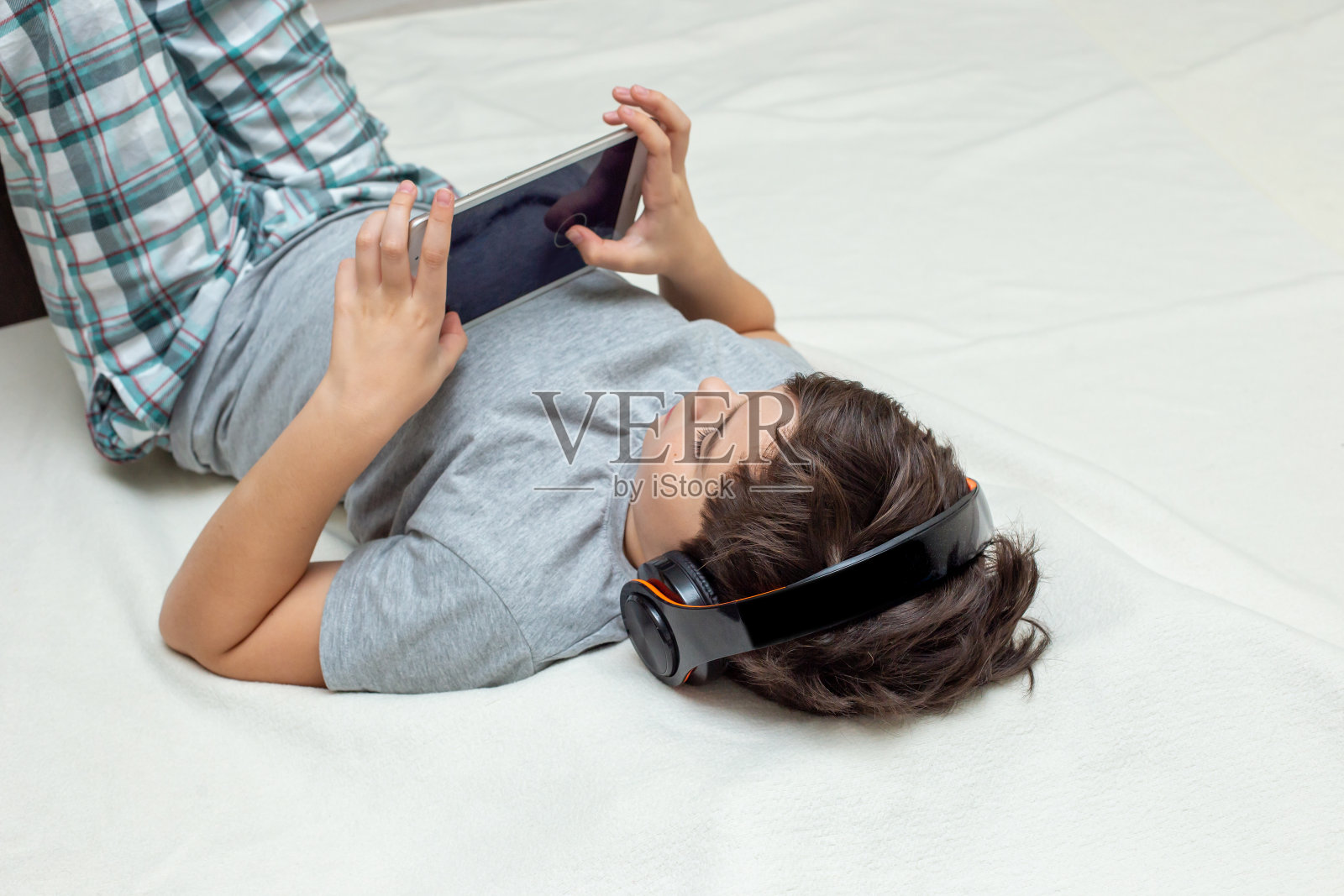 一个十几岁的男孩躺在床上玩电子平板电脑照片摄影图片