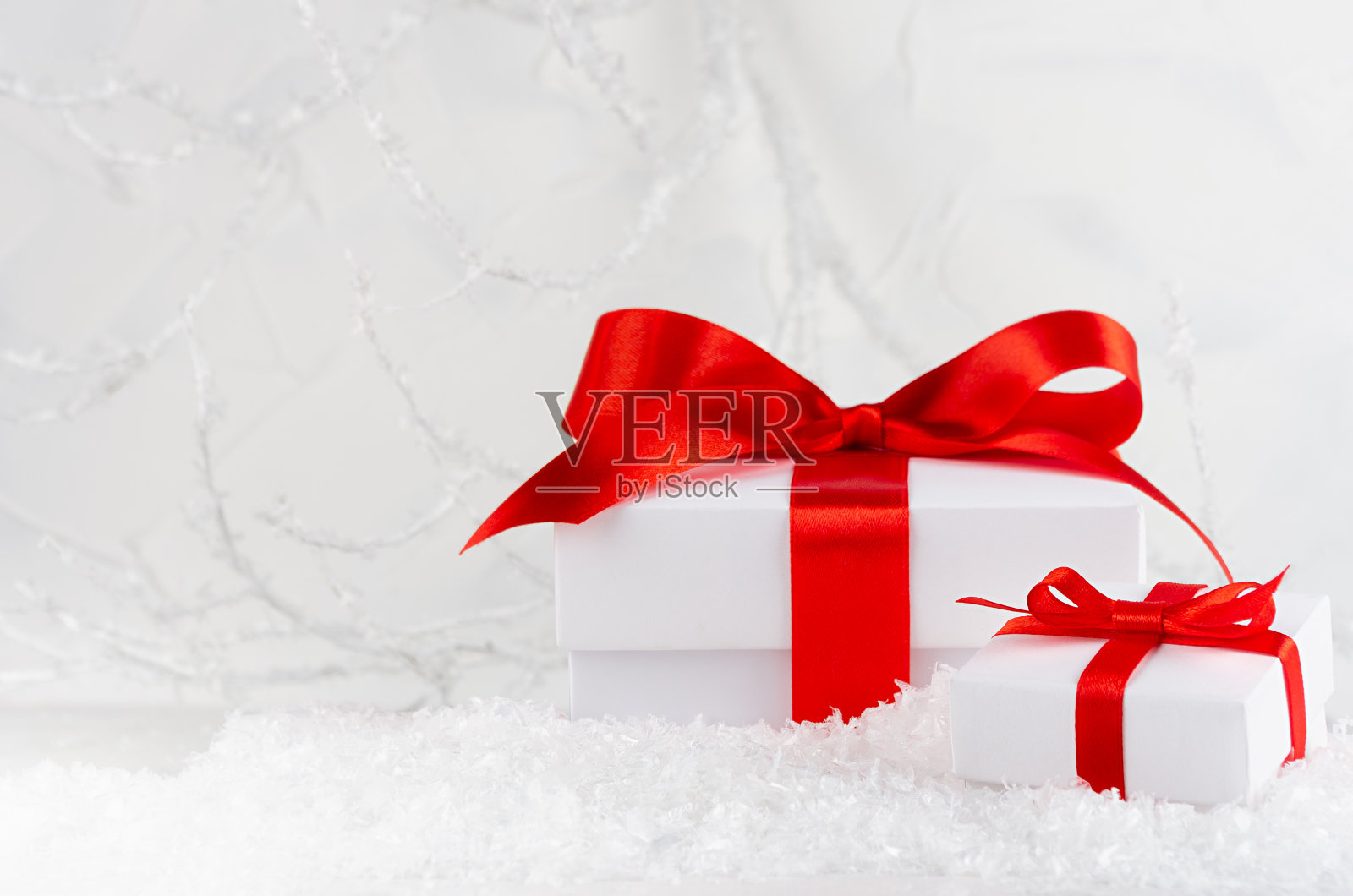 优雅的白色节日背景与红丝带的礼品盒和装饰冬天霜森林与白色的树枝和雪,复制空间,特写。圣诞节日的背景。照片摄影图片