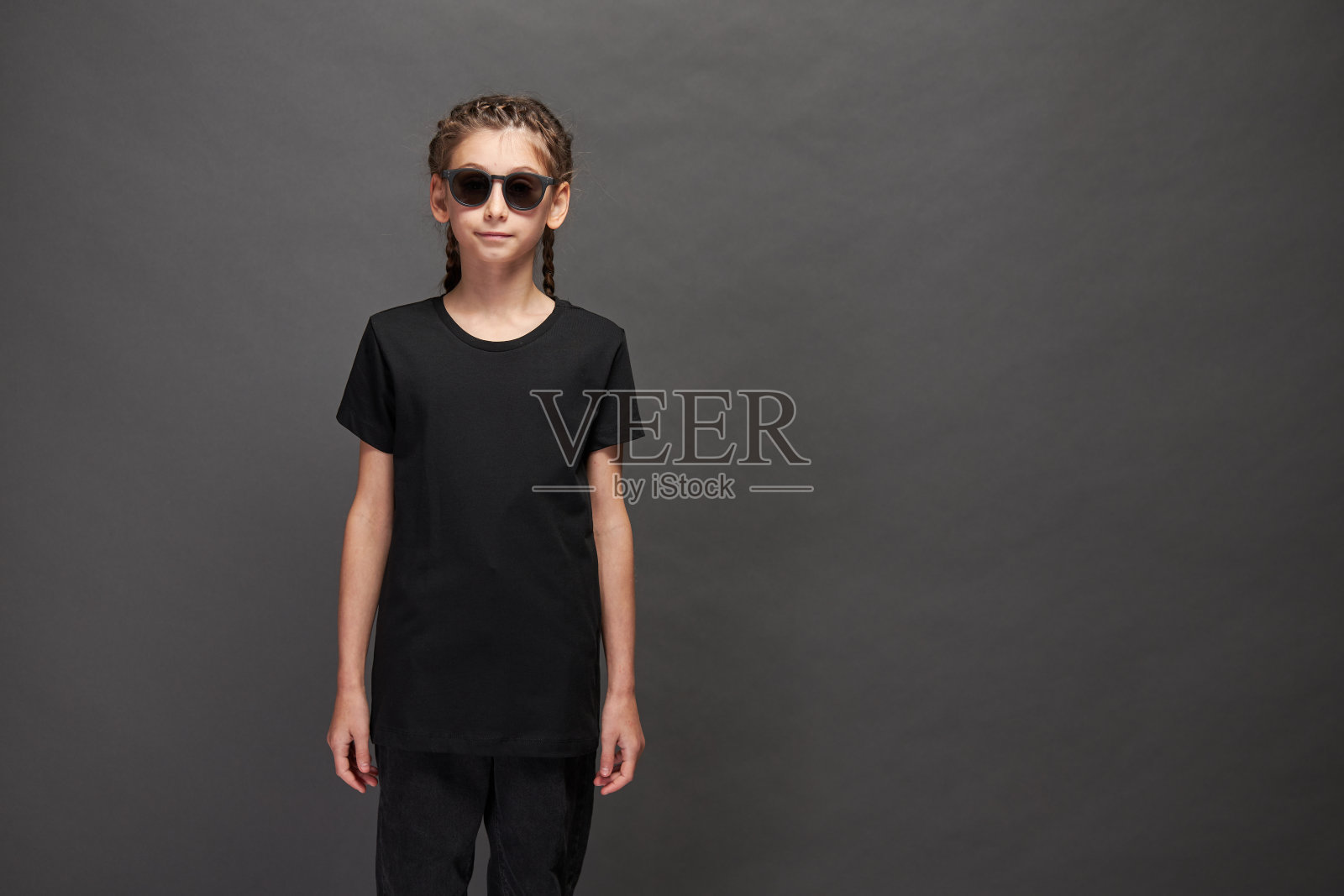 小女孩穿着黑色t恤与空间为您的标志或设计在工作室的灰色背景与太阳镜照片摄影图片