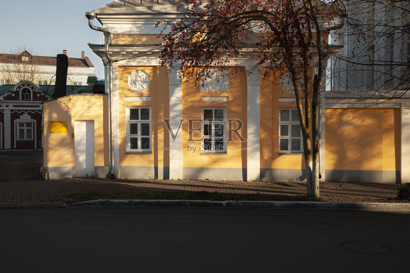 在树荫下的黄色建筑。照片摄影图片