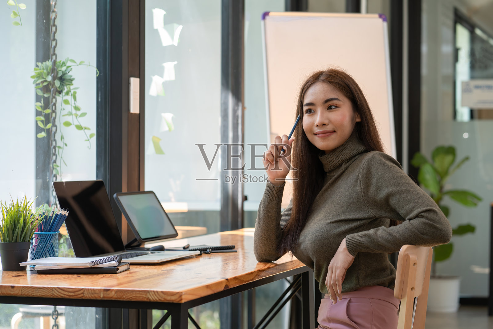 漂亮的年轻亚洲女商人在办公室里用笔记本电脑一边拿着铅笔一边思考照片摄影图片