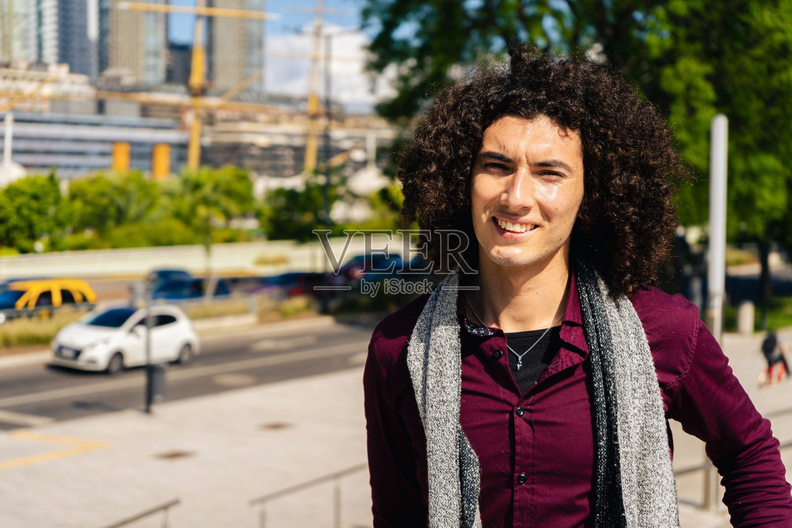 一个微笑的卷发年轻拉丁美洲人的肖像穿着一件衬衫在街上。照片摄影图片