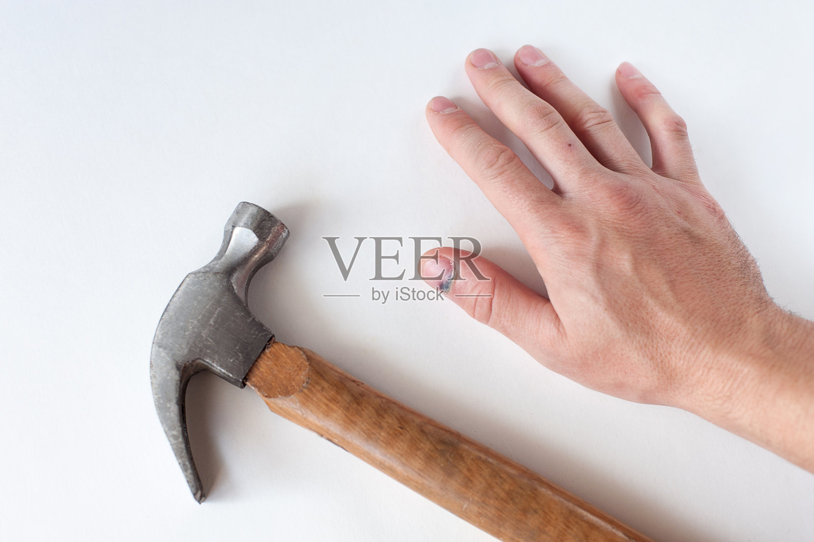 在浅色背景上有一只手和一把锤子。一根被锤子击打的手指上有蓝色的钉子照片摄影图片