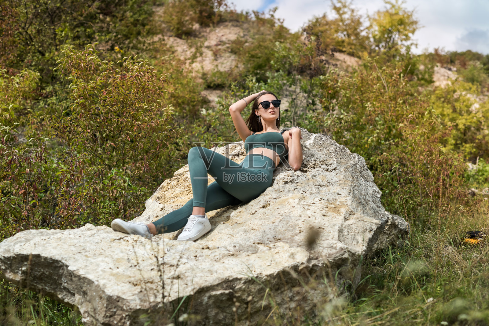 漂亮苗条的女孩坐在山上的一块石头上,过暑假照片摄影图片