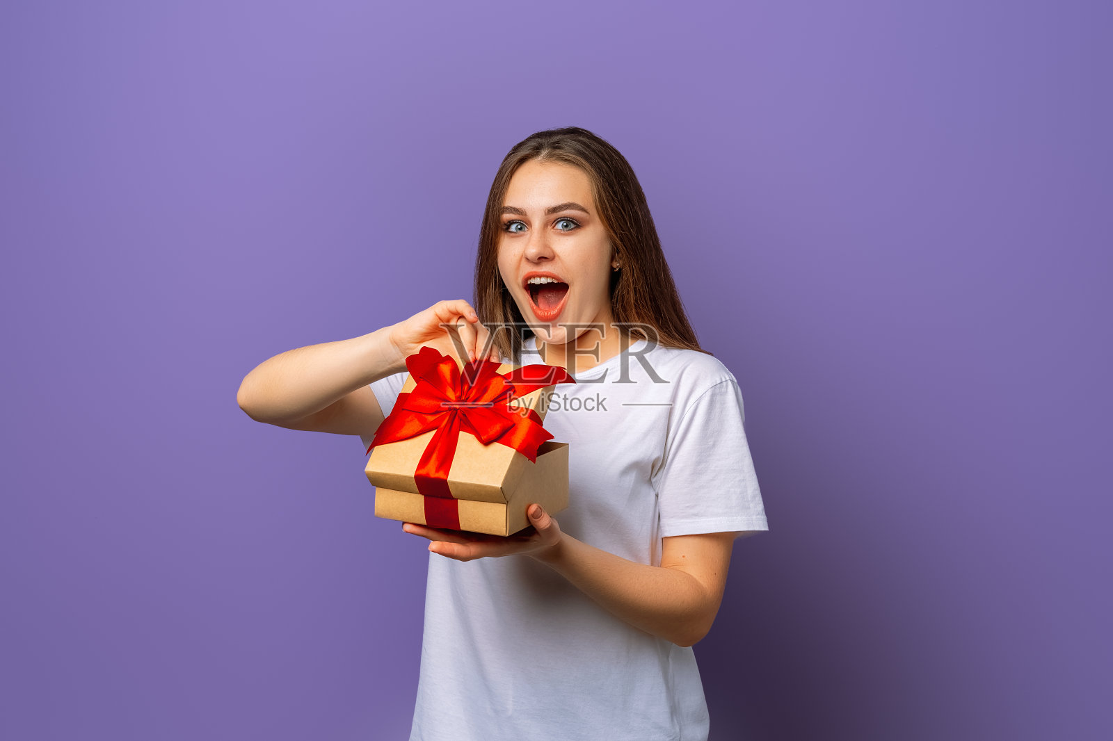 情绪激动的黑发年轻女子打开装有生日礼物的盒子,脸上带着狂喜的表情,张大嘴巴,对这样的惊喜感到感激照片摄影图片