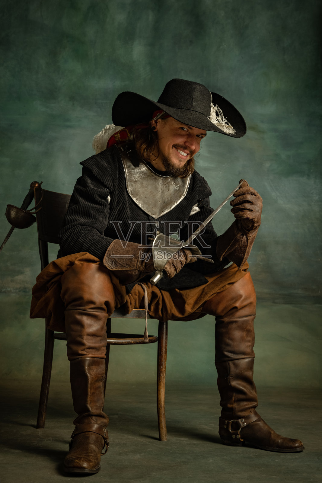 野蛮可怕的人的肖像,中世纪海盗在古着服装坐和持剑孤立在黑暗的背景。照片摄影图片