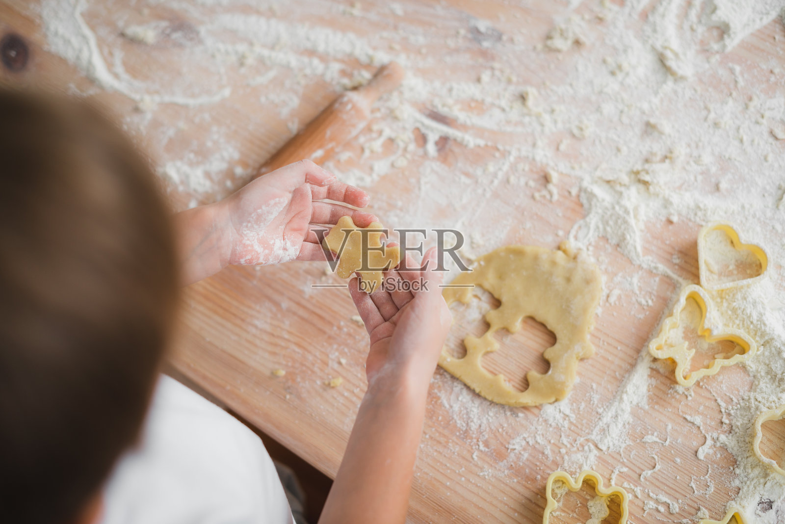 家庭烹饪概念:孩子们的手从生面团中切出熊形状的空白饼干的特写镜头。照片摄影图片