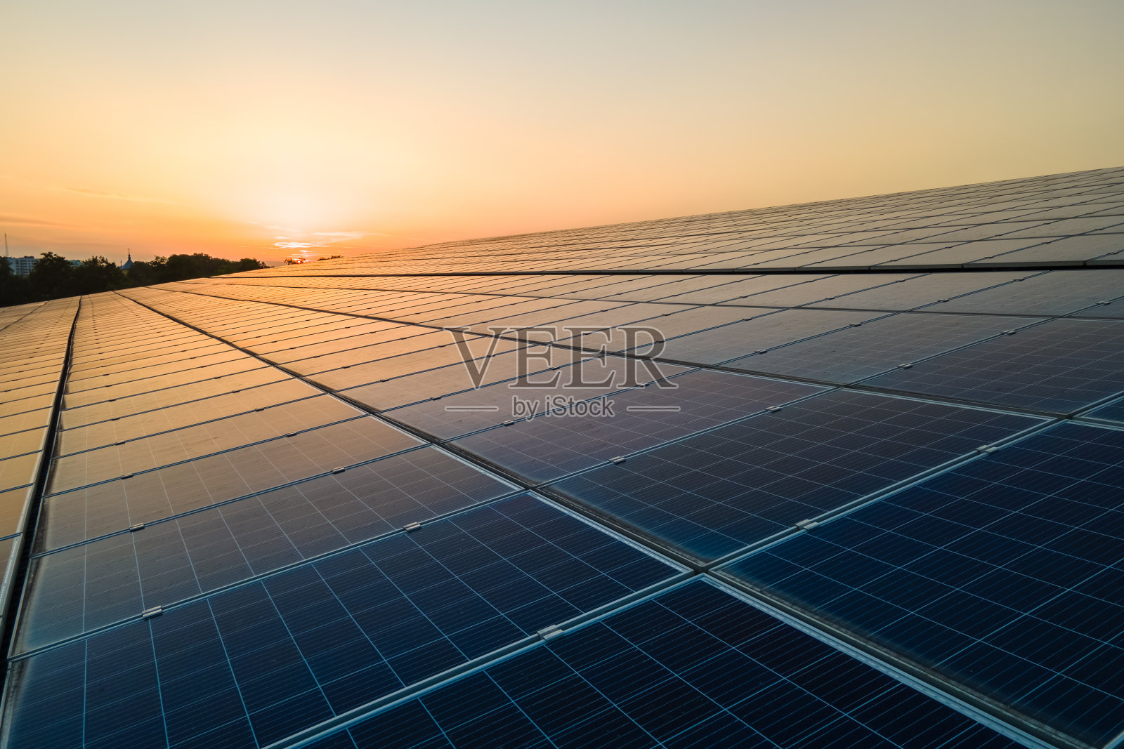 安装在建筑屋顶的蓝色光伏太阳能板,在日落时产生清洁的生态电力。生产可再生能源的理念。照片摄影图片