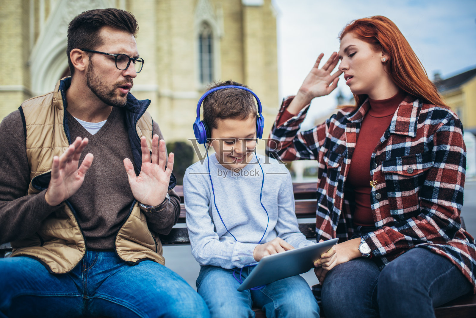 一家人坐在长凳上,放松地使用电子产品,浏览互联网。照片摄影图片