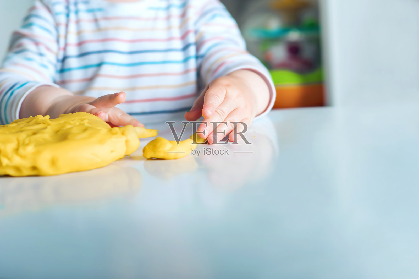 蹒跚学步的男孩在游戏室里玩黄色橡皮泥。照片摄影图片