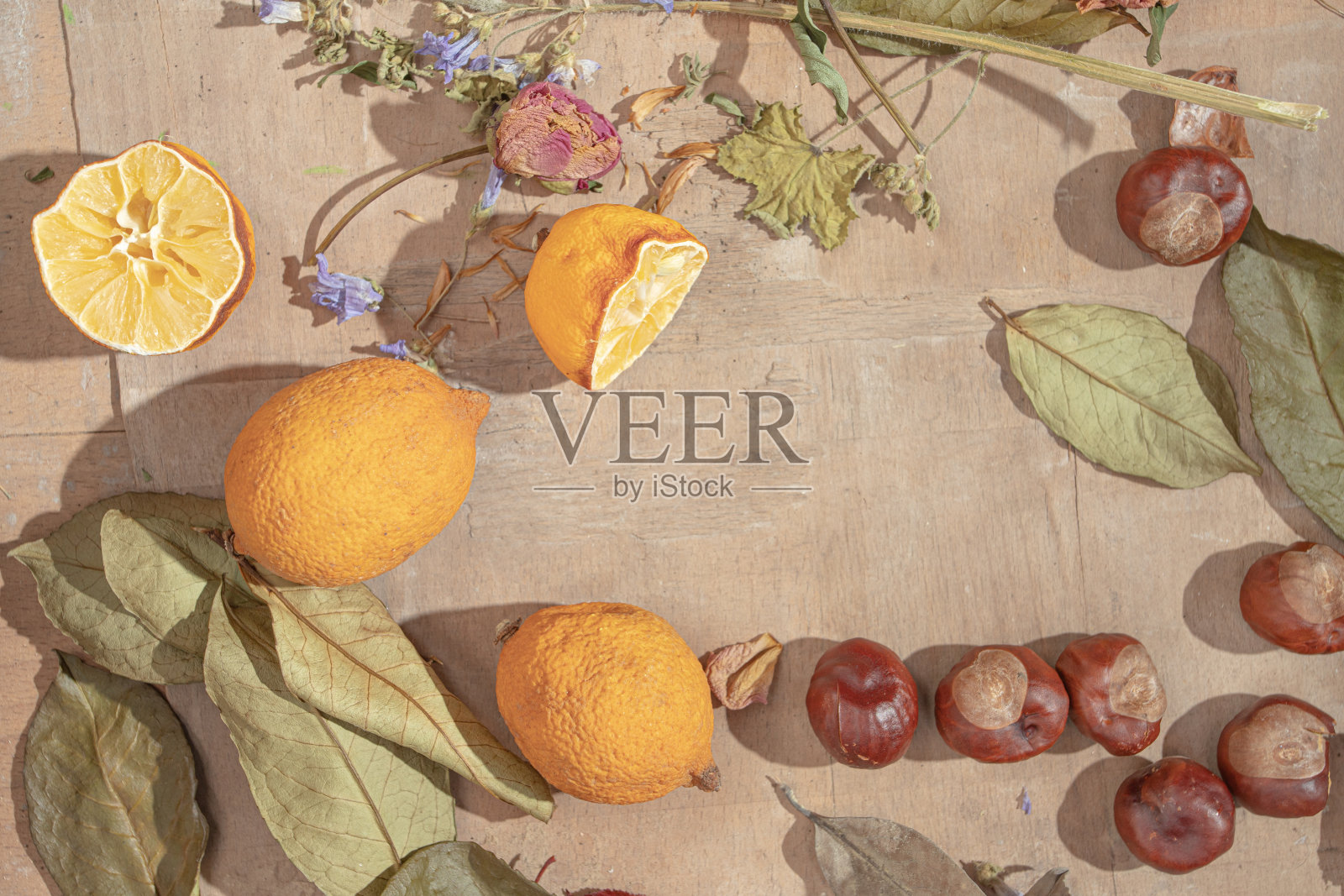 干树叶、花、挤过的柠檬和栗子放在一张简陋的旧木桌上。有空地的平铺布置。秋冬季节概念。照片摄影图片