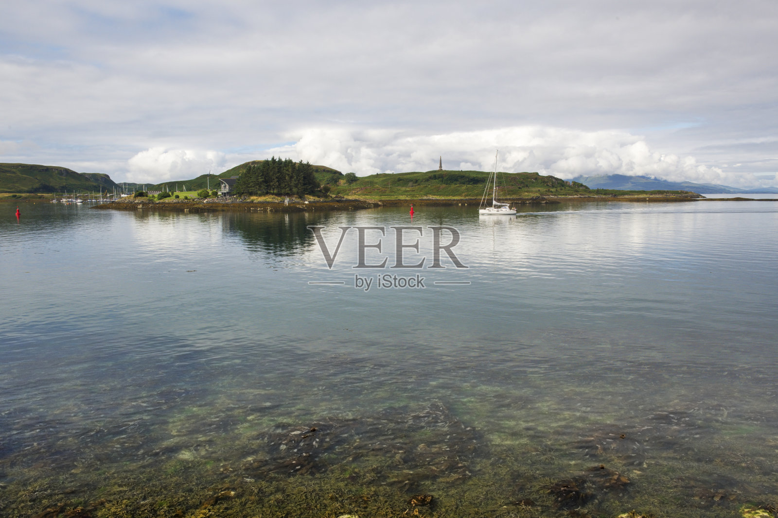 一艘游艇穿过清澈的水域驶向苏格兰阿吉尔郡奥班湾的码头。照片摄影图片