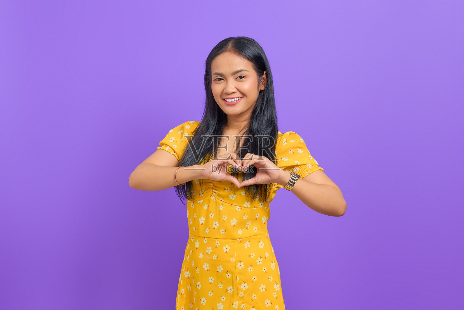 微笑的年轻亚洲女子用两只手表示心意,并看着相机在紫色的背景照片摄影图片