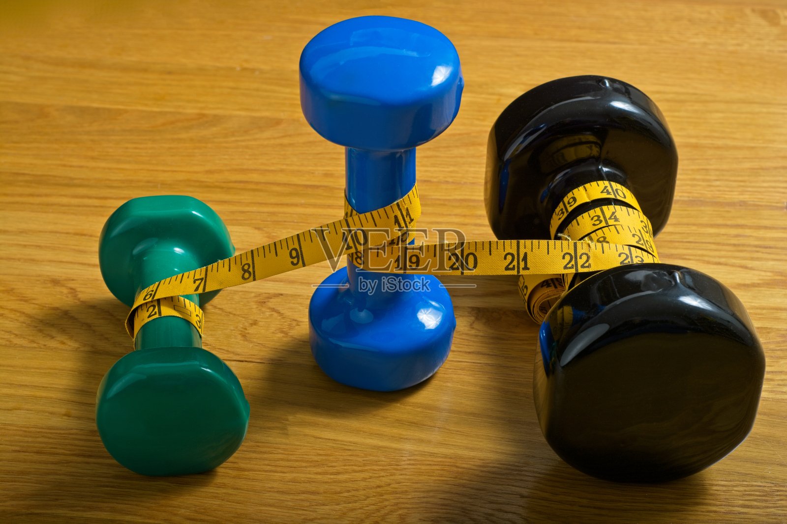 三个哑铃按重量排列,中间重量用黄色卷尺包着站着照片摄影图片