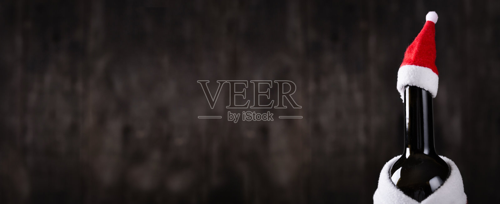 葡萄酒瓶在圣诞老人的帽子和服装在木制的乡村背景。长长的横幅照片摄影图片