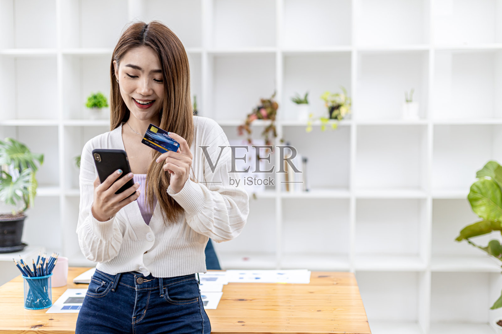 漂亮的亚洲女人手持智能手机和信用卡,填写信用卡信息以支付商品和服务费用,在线购物概念照片摄影图片