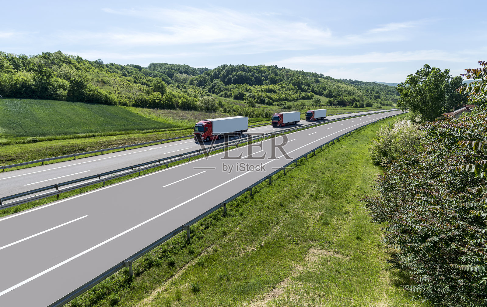 一群卡车在草地和茂密森林之间的公路上行驶。照片摄影图片