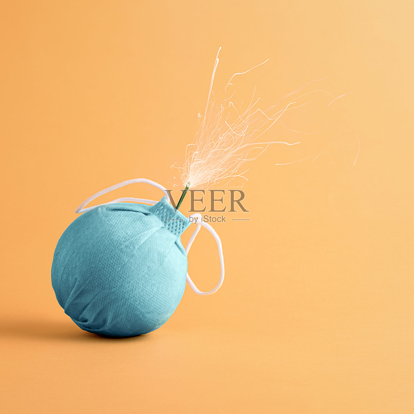 创意大流行的概念。橙色背景,炸弹形状,引信燃烧的医用口罩。照片摄影图片