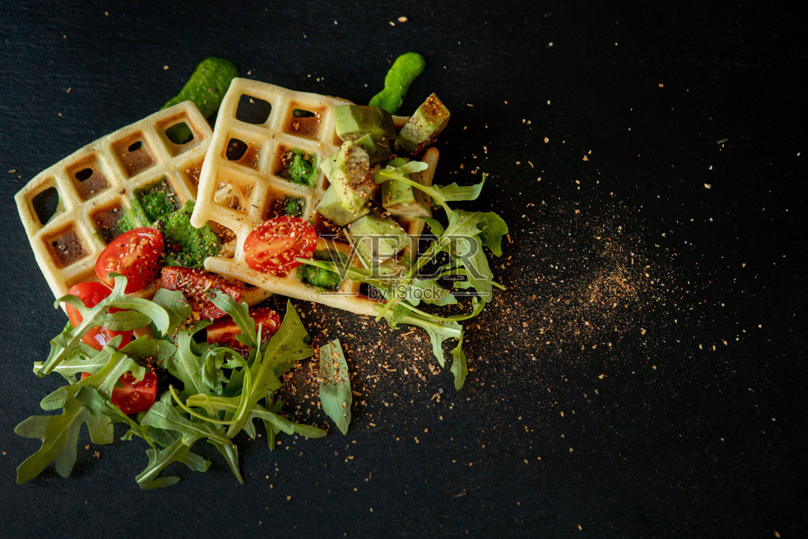 新鲜出炉的比利时华夫饼,配芝麻菜、西红柿和牛油果,放在黑色的盘子里。美味的华夫饼。早餐的概念。健康的早餐照片摄影图片