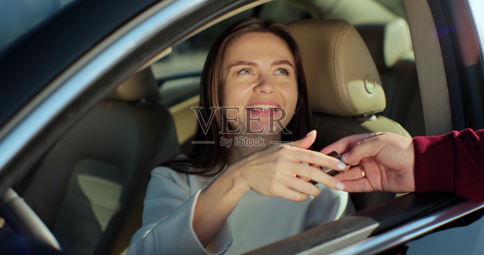 一名男子把钥匙交给坐在车里的年轻女子。快乐的女高管从新车里拿到钥匙。快乐的车主在现代沙龙购买交通工具。照片摄影图片