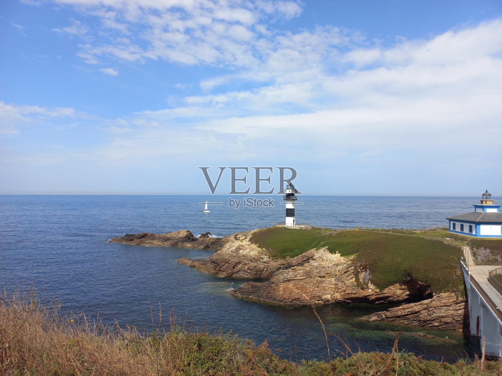 一艘在西班牙里巴迪奥海岸灯塔后面航行的船照片摄影图片