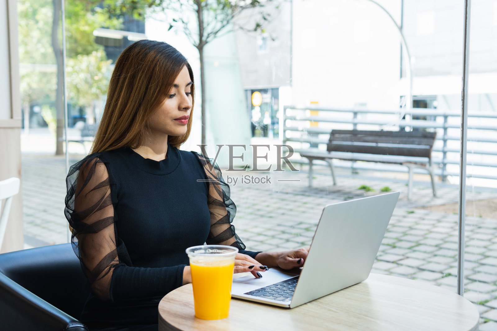 积极的年轻女商人一边用笔记本电脑工作,一边坐在喝橙汁的咖啡店里。学生与商业概念照片摄影图片