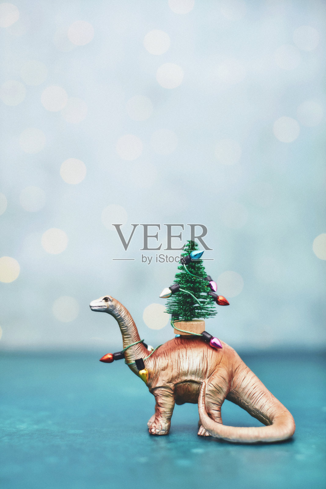 圣诞背景与可爱的金色恐龙携带小圣诞树包裹在节日灯照片摄影图片