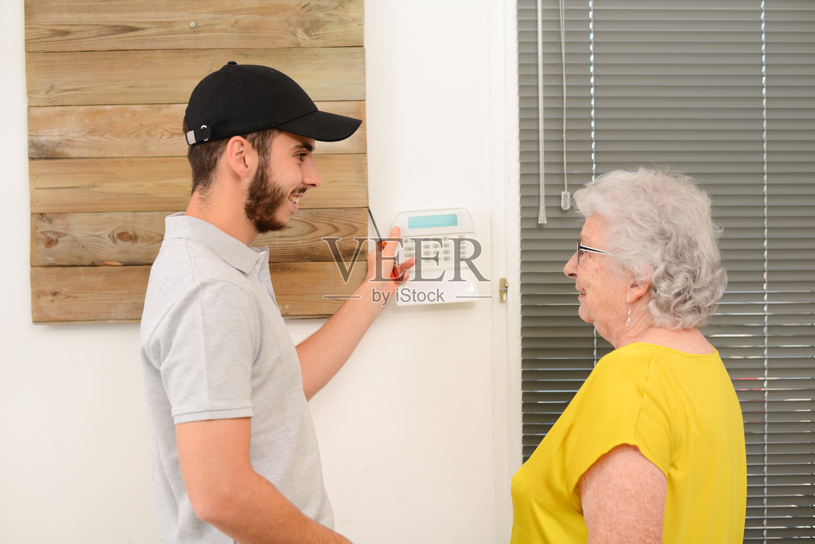 一名英俊的年轻男子在一名老年妇女家中安装了房屋安全防盗摄像头和警报器照片摄影图片
