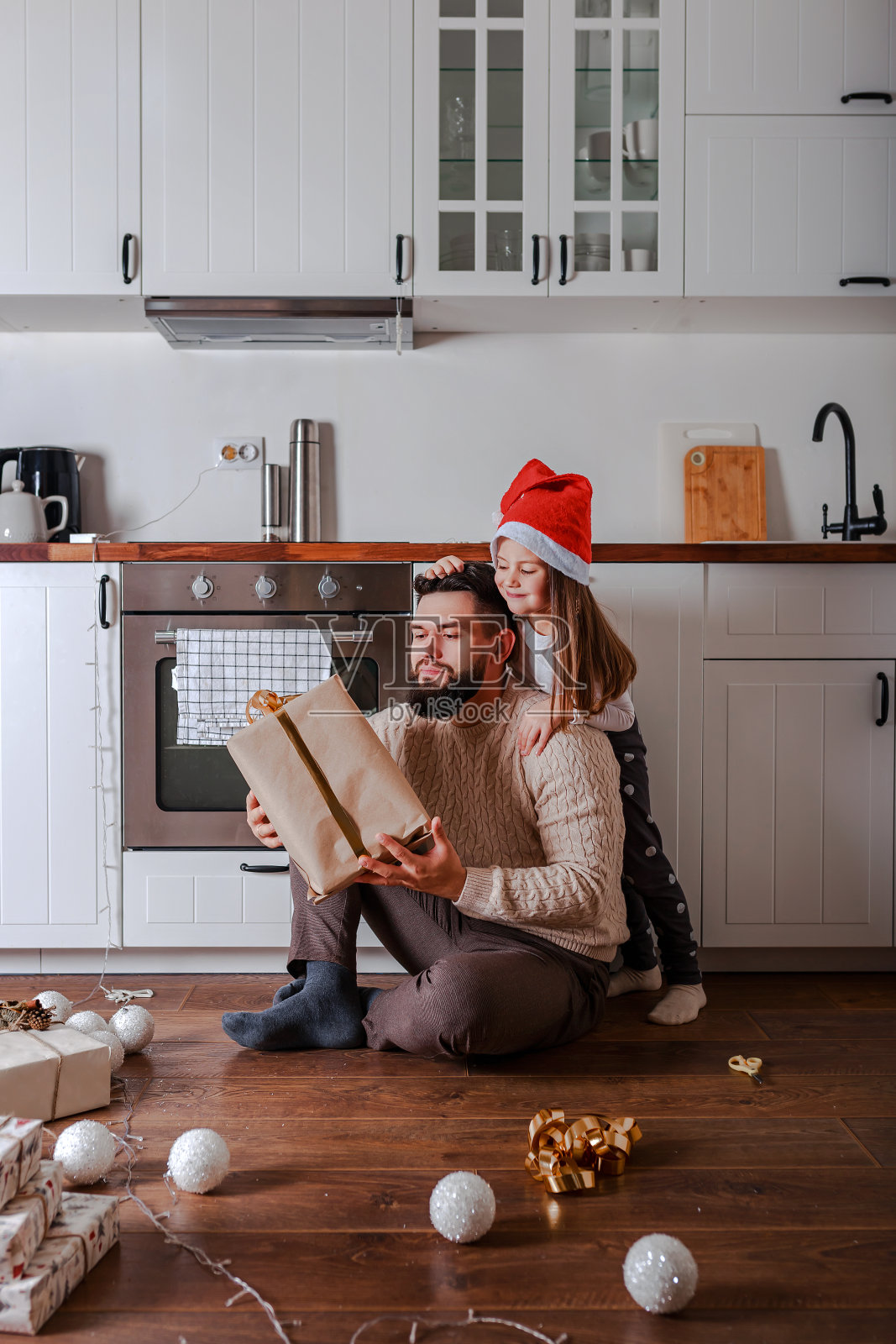 父亲和女儿在家装饰圣诞礼物。女儿抱着圣诞老人的帽子。在家过圣诞节。照片摄影图片