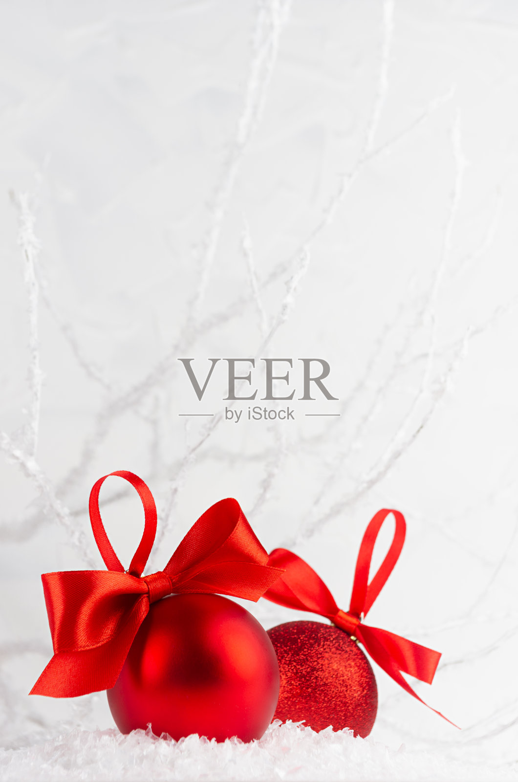 圣诞装饰——两个富有红色光泽的闪光球用缎子丝带装饰着柔和的光,白色的冬天森林用霜冻的树枝,雪,复制空间,垂直。喜庆的新年背景。照片摄影图片