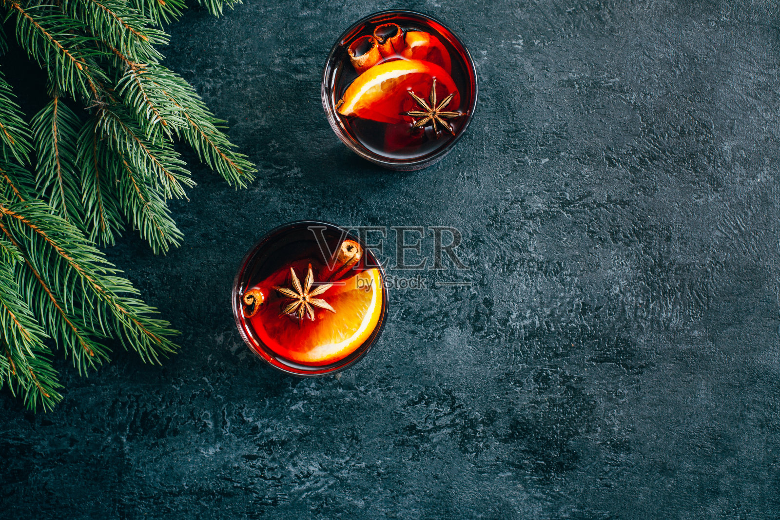 这是一杯热饮的顶视图:在透明的玻璃杯中加入橙和八角,背景是深色的混凝土,装饰着圣诞树的树枝,有文字的自由空间照片摄影图片