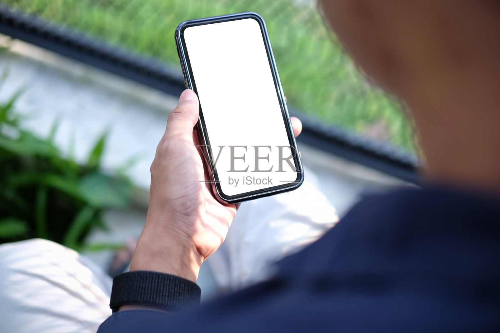 一个年轻人坐在花园里用智能手机。照片摄影图片