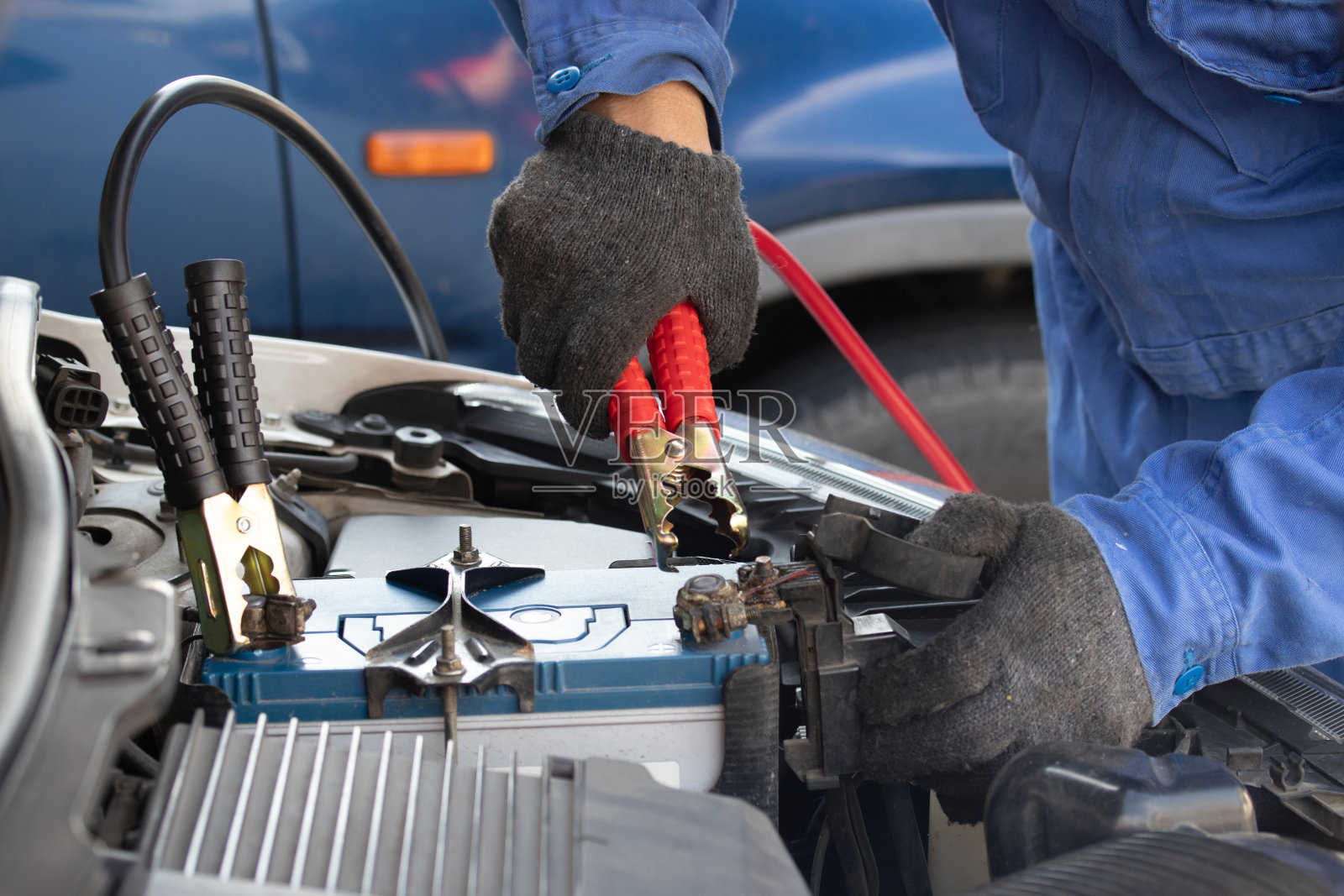 近手机械师汽车服务电池与电力通过跨接线。服务工作以专业技师的理念进行。照片摄影图片