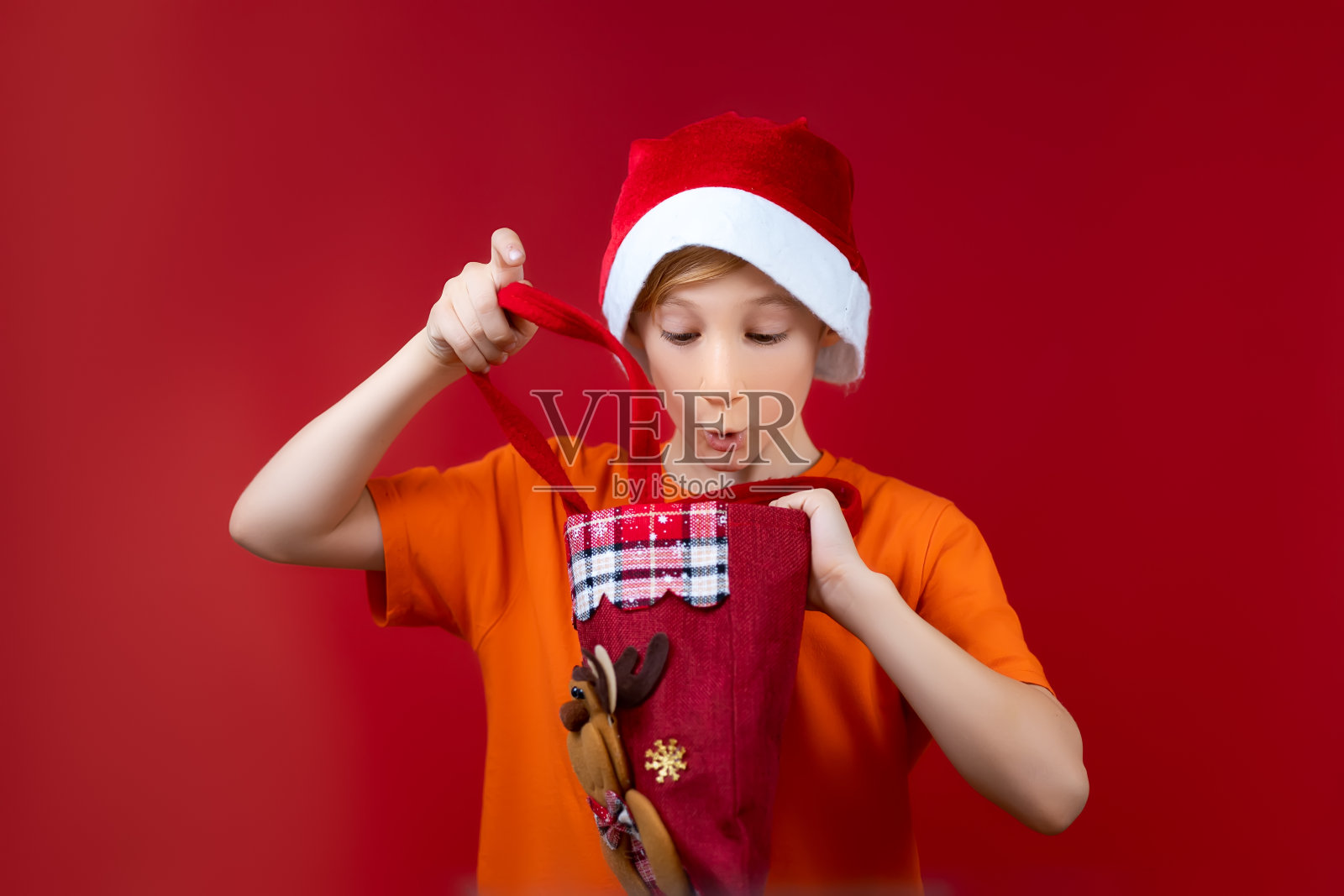 一个在红色圣诞背景上戴圣诞帽的男孩照片摄影图片