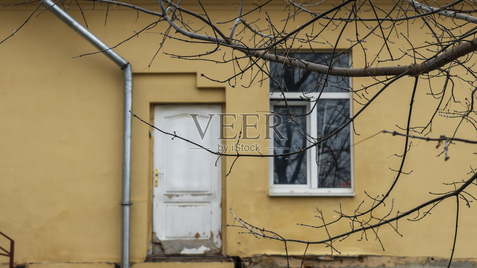 离焦的白色旧木门在黄色带窗户的旧墙的背景上无处可寻。照片摄影图片