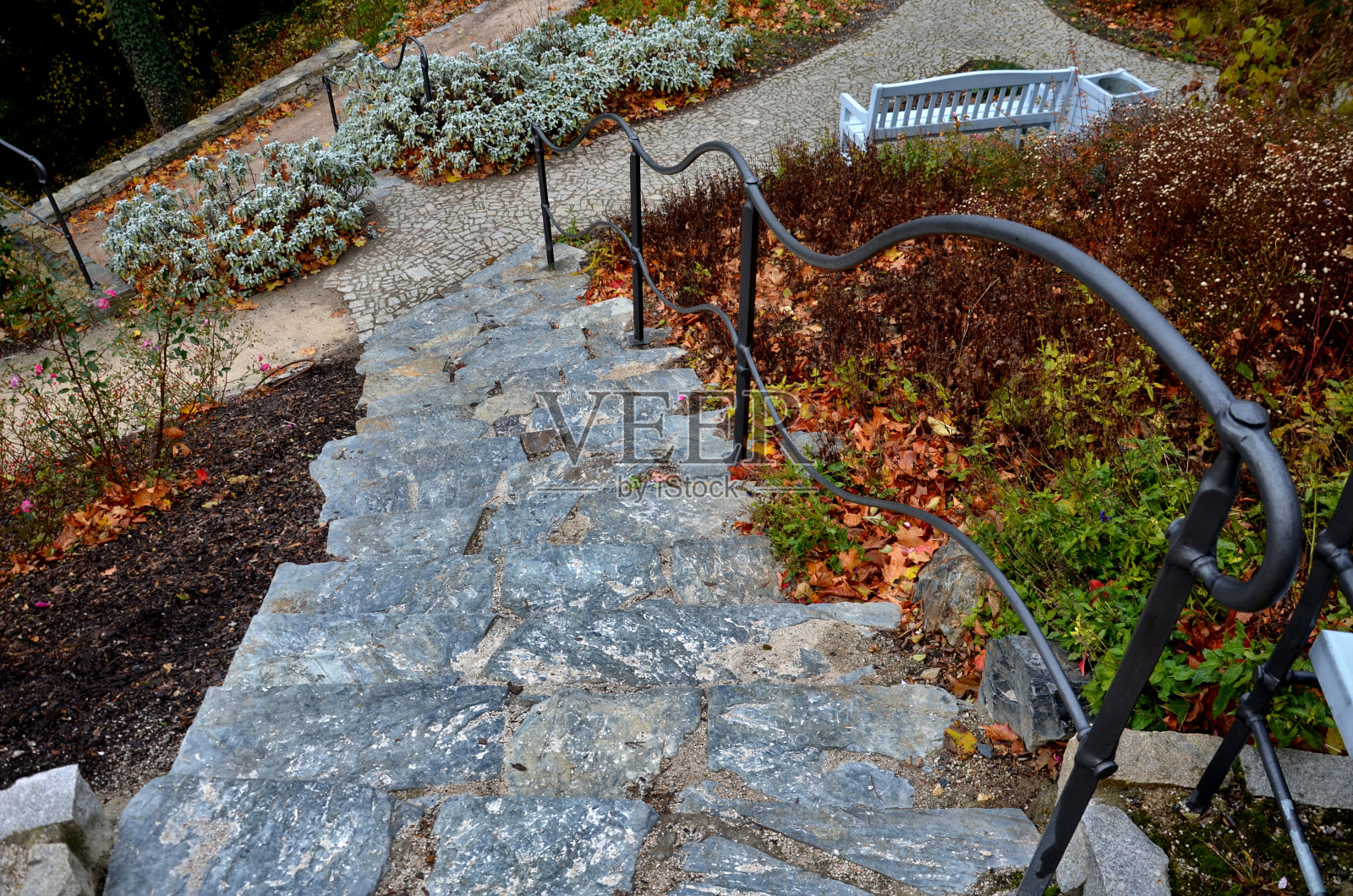 把石头堆在楼梯表面。公园内有棕色和灰色斑岩。鹅卵石小径,阶地,鼠尾草和栏杆锻造成波浪形状。拱形长凳和饮水机照片摄影图片